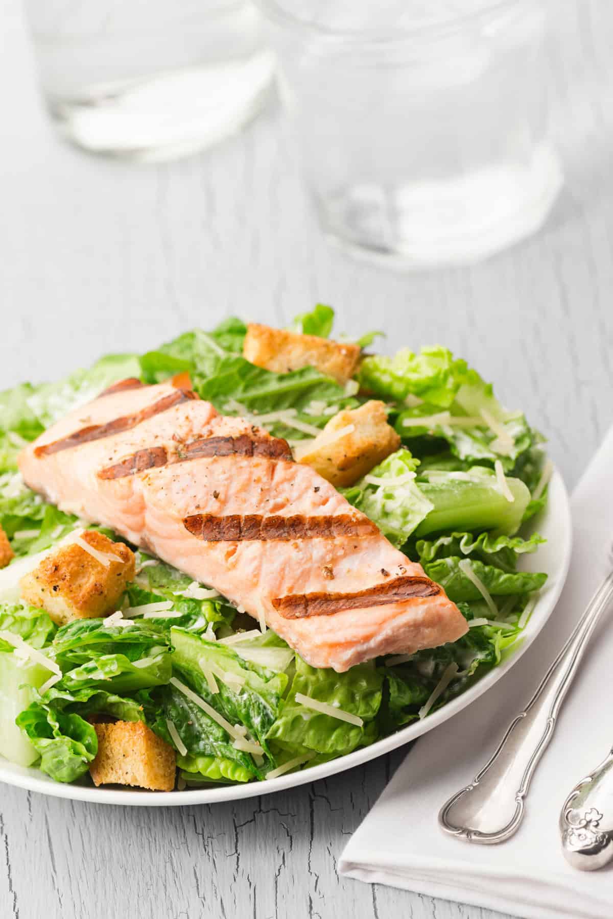 A piece of grilled salmon sitting on a bed of Caesar salad, served in a white shallow bowl.