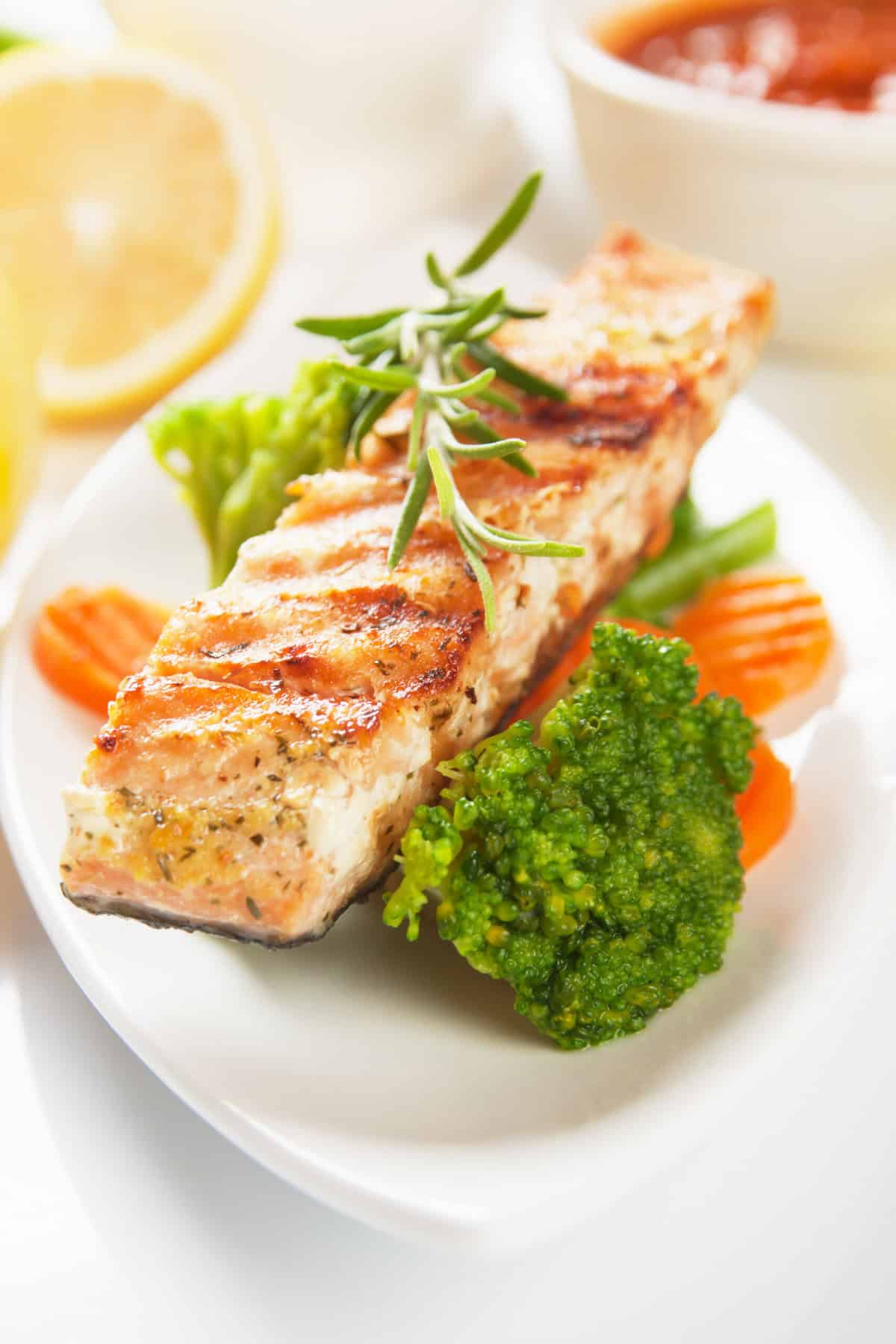 Grilled salmon, with steamed vegetables, served on a white oval plate.
