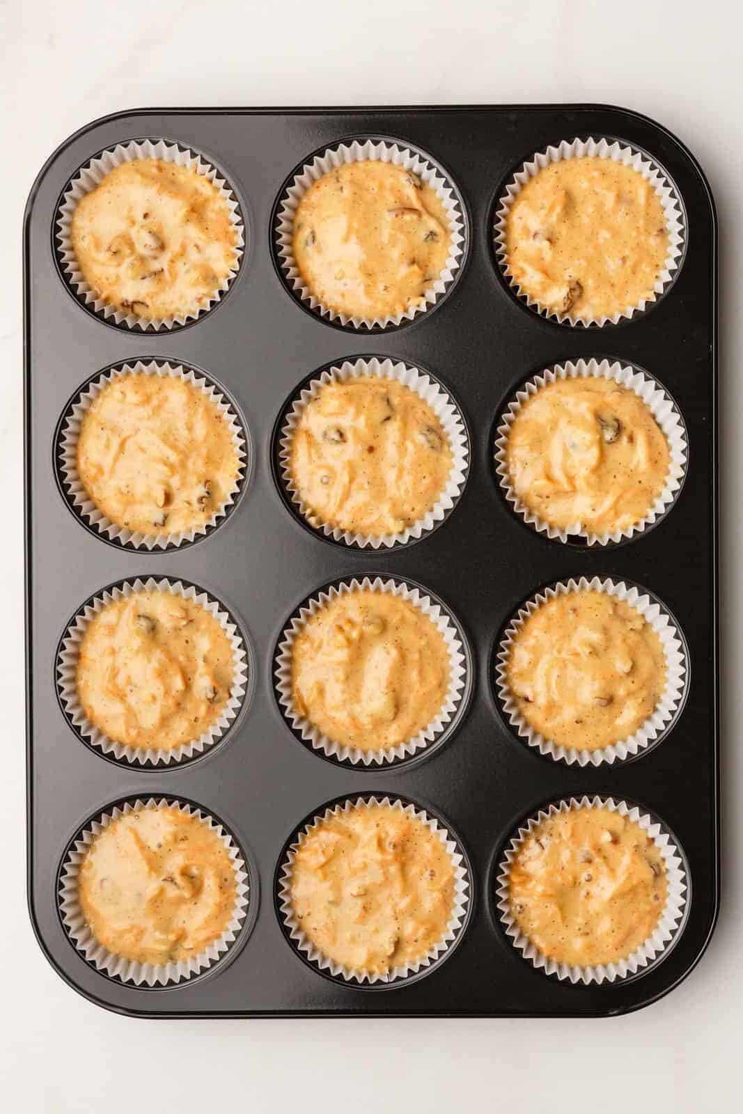 top down image of 12 morning glory muffin batter prepared in a muffin tin. 
