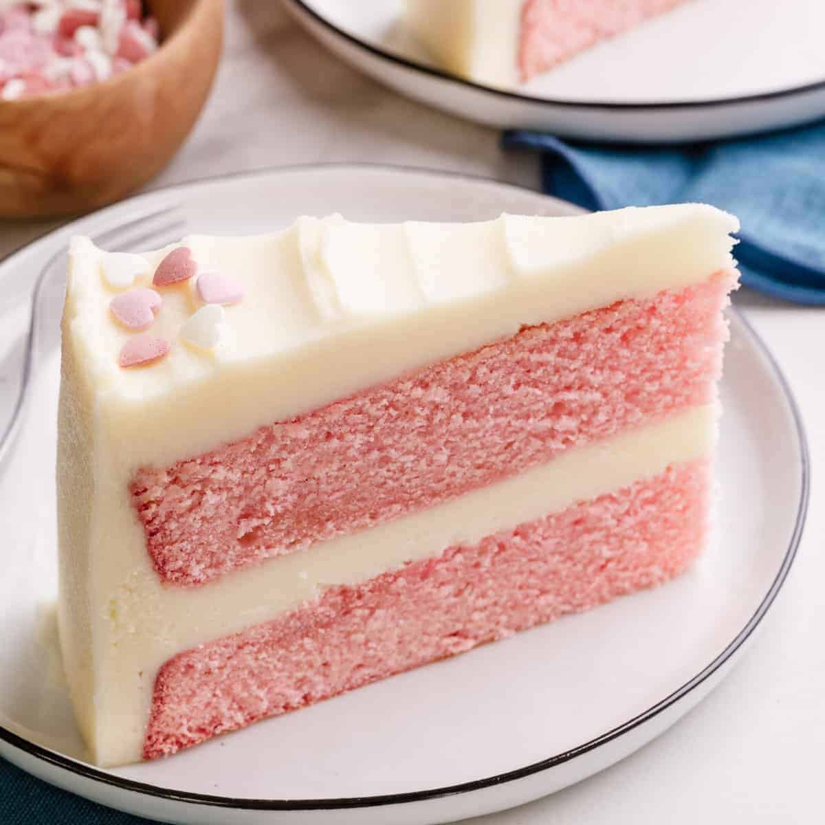 A slice of double layer pink velvet cake with buttercream frosting.
