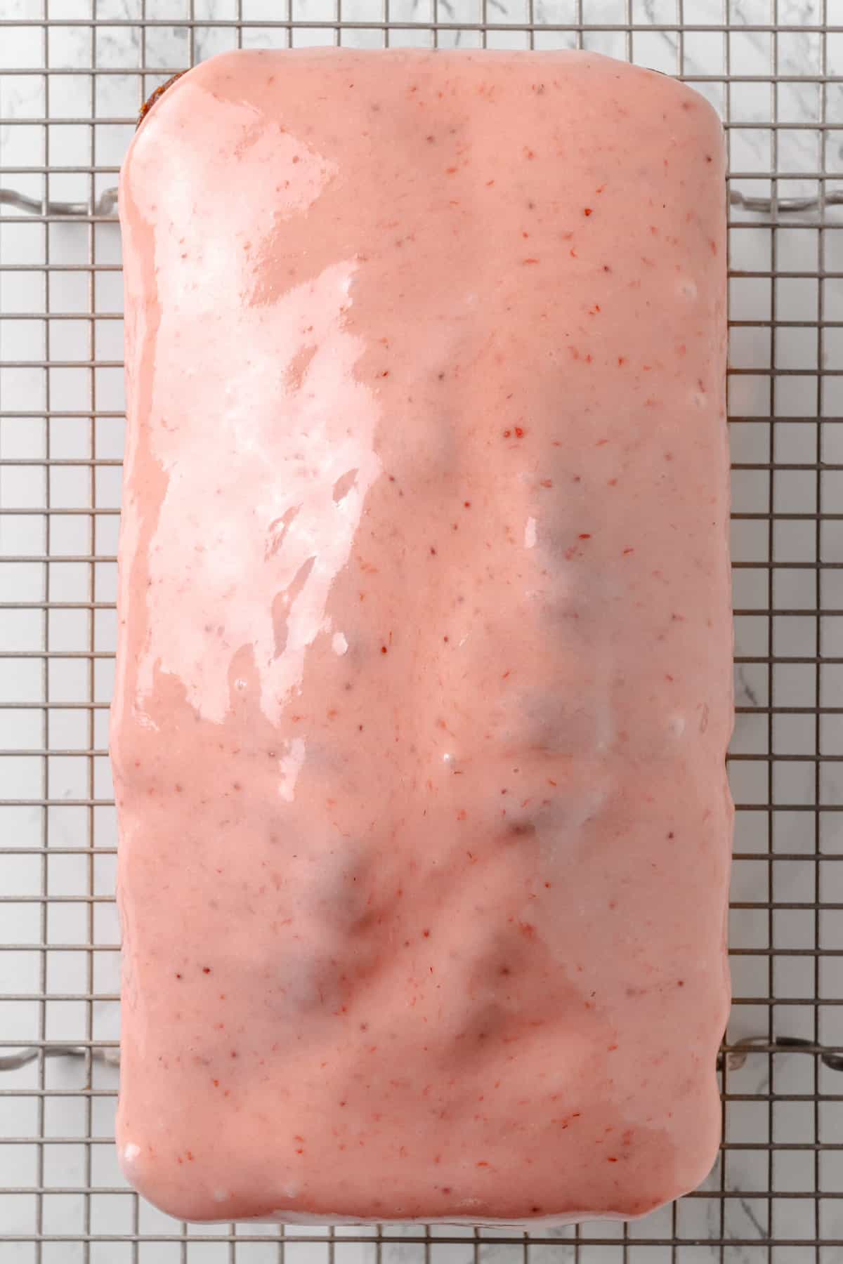 Top down image of a glazed strawberry pound cake cooling on a wire rack.