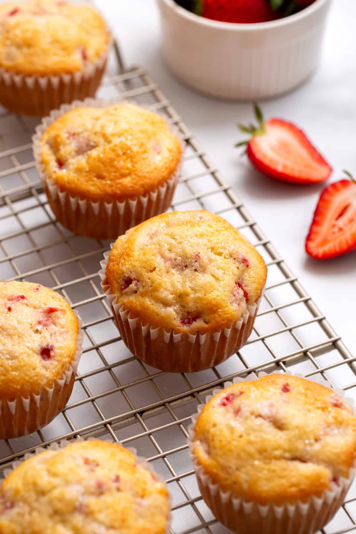 Strawberry muffins sitting on a wire cooling rack.
