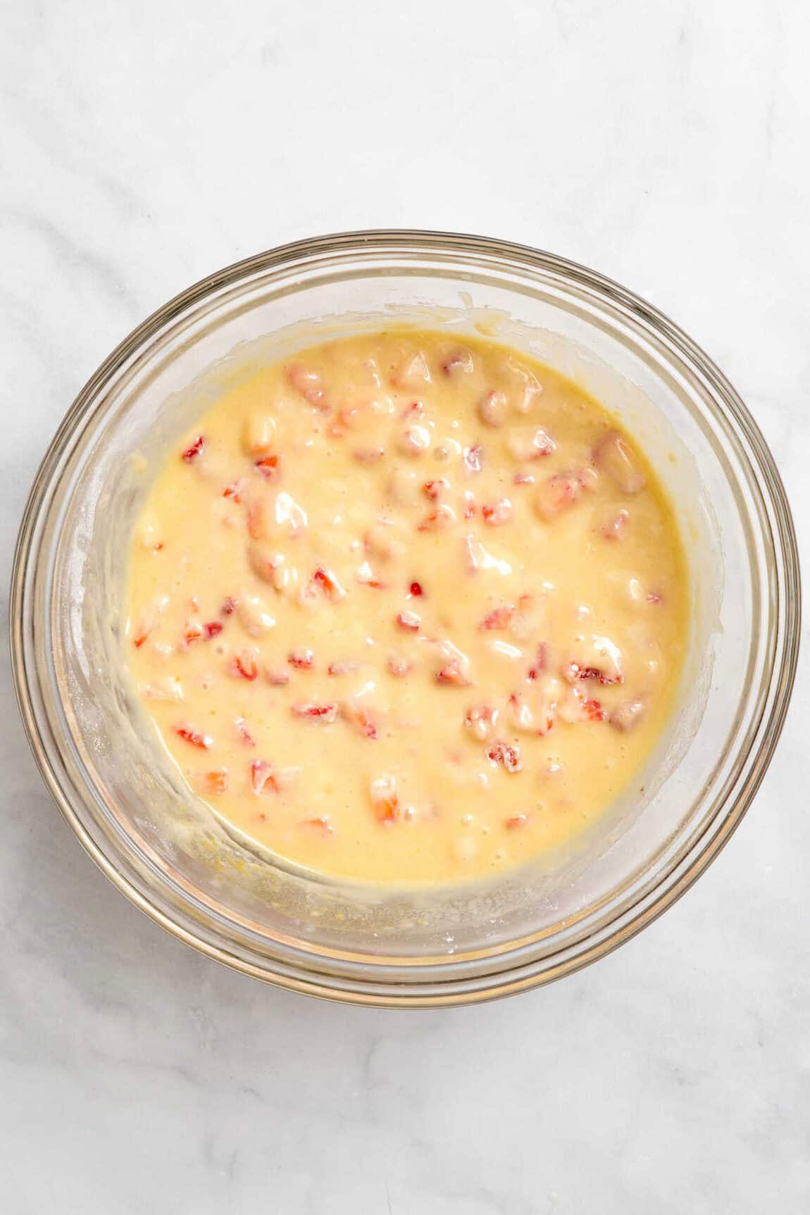 Top down image of strawberry muffin batter in a large glass bowl.