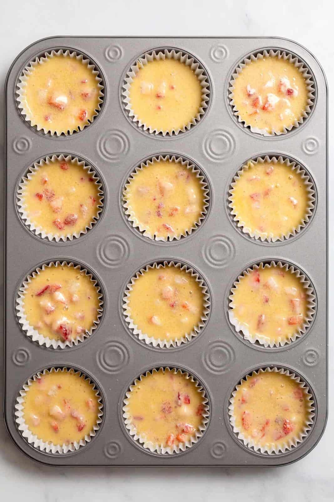 Top down image of a 12 count muffin tin lined with strawberry muffin batter.