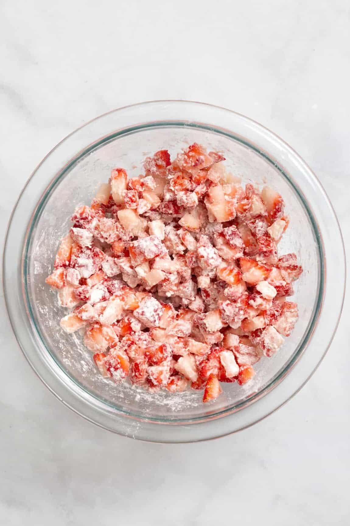 Top down image of a large glass bowl with cut strawberries coated in flour.