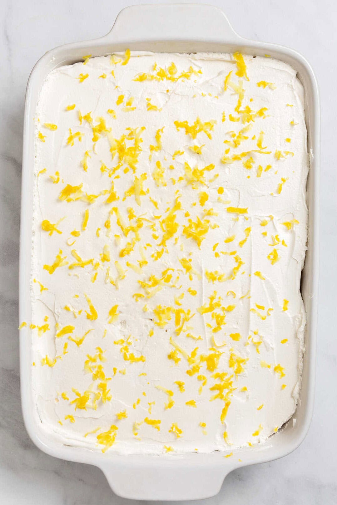 Top image of a 9 x 13 baking dish with lemon poke cake and lemon frosting.