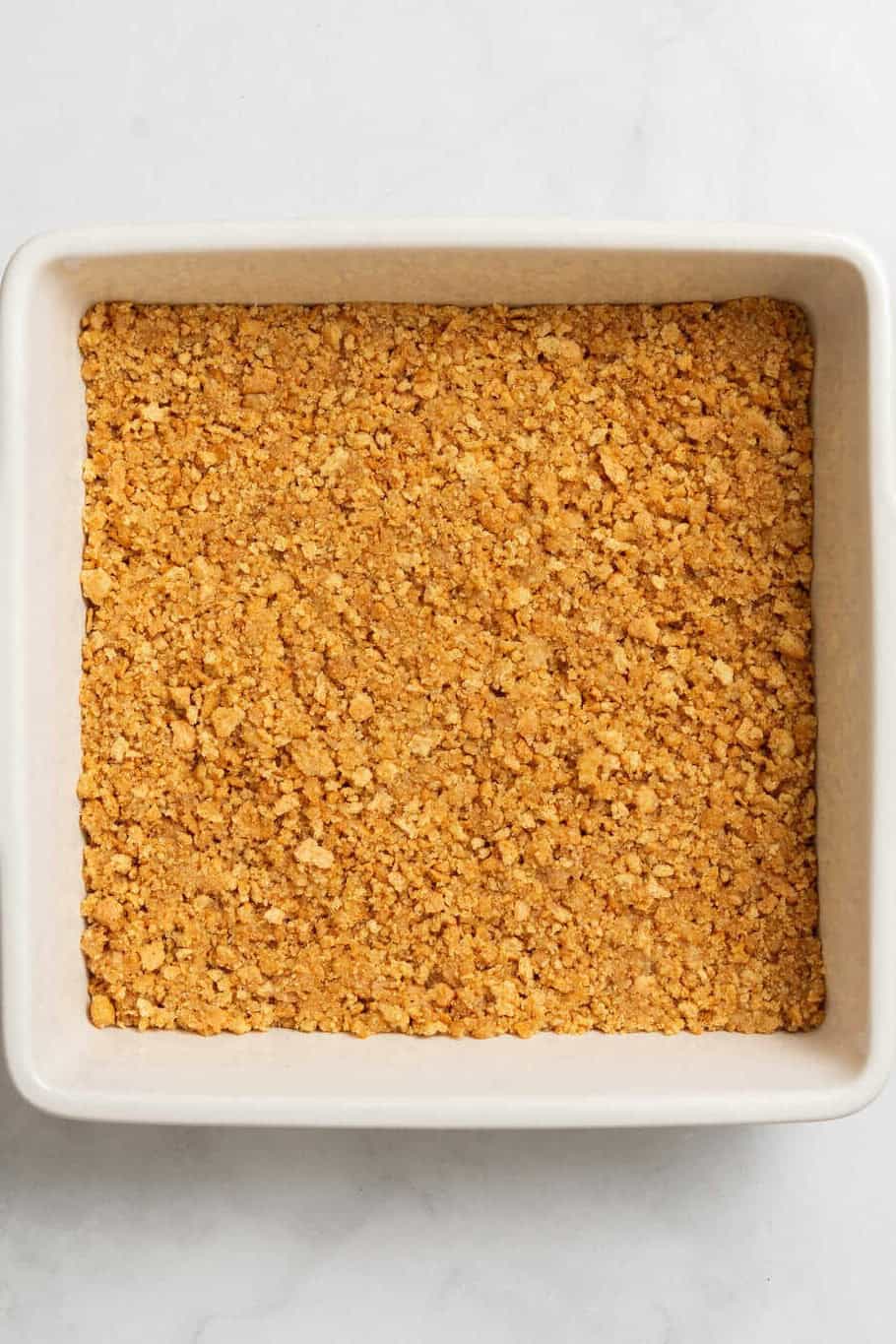 Top down image of an 8 x 8 baking dish with graham cracker crust press to the bottom of the pan.