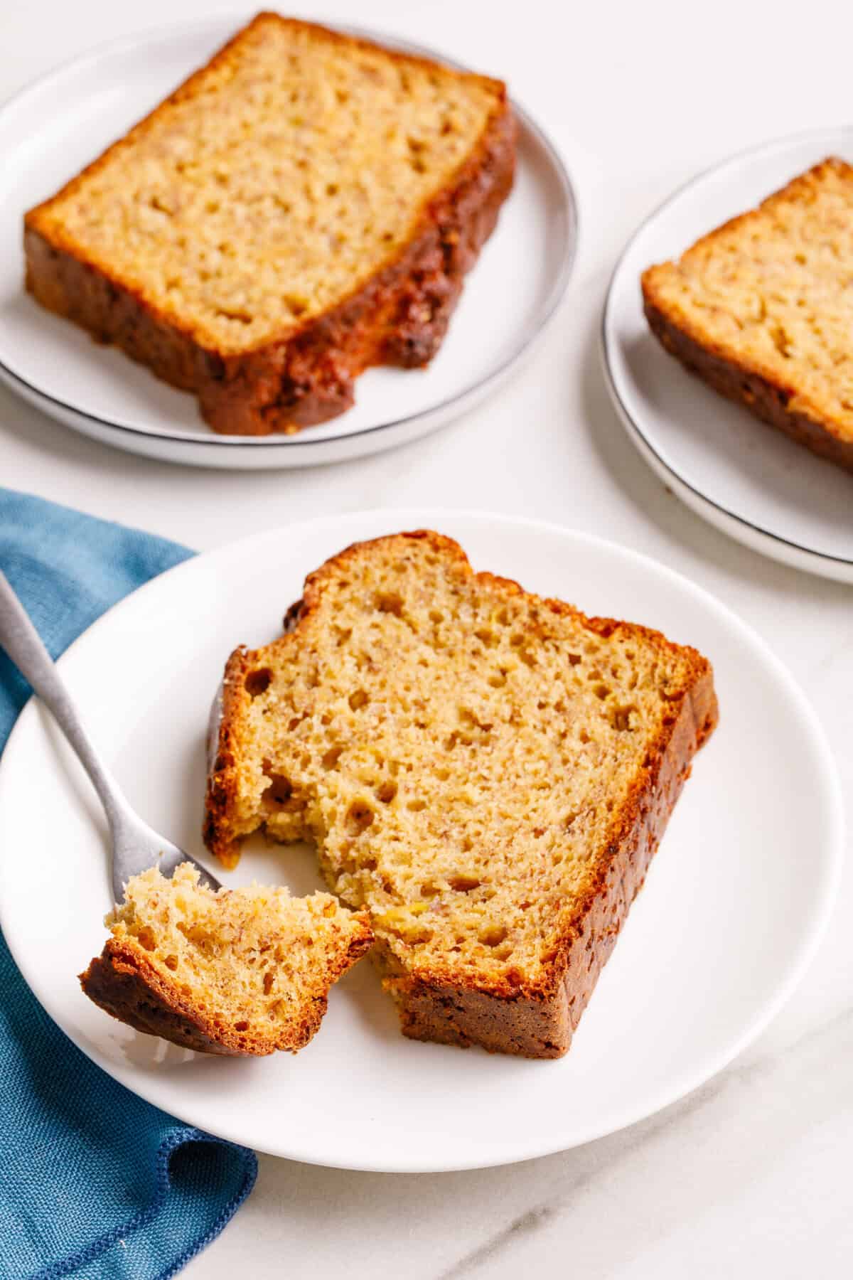 Sliced 4-ingredient banana bread on white serving plates, a piece of 4-ingredient banana bread on a metal fork.