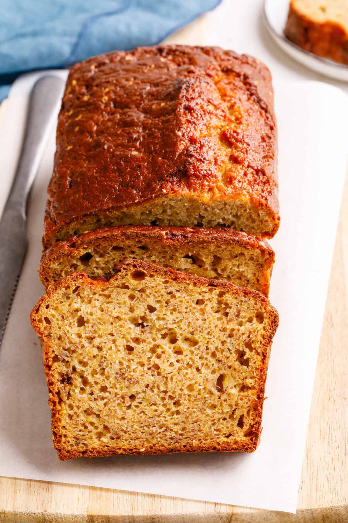 Close up of 4-Ingredient banana bread on a sheet of parchment paper atop a wooden cutting board with two slices cut.