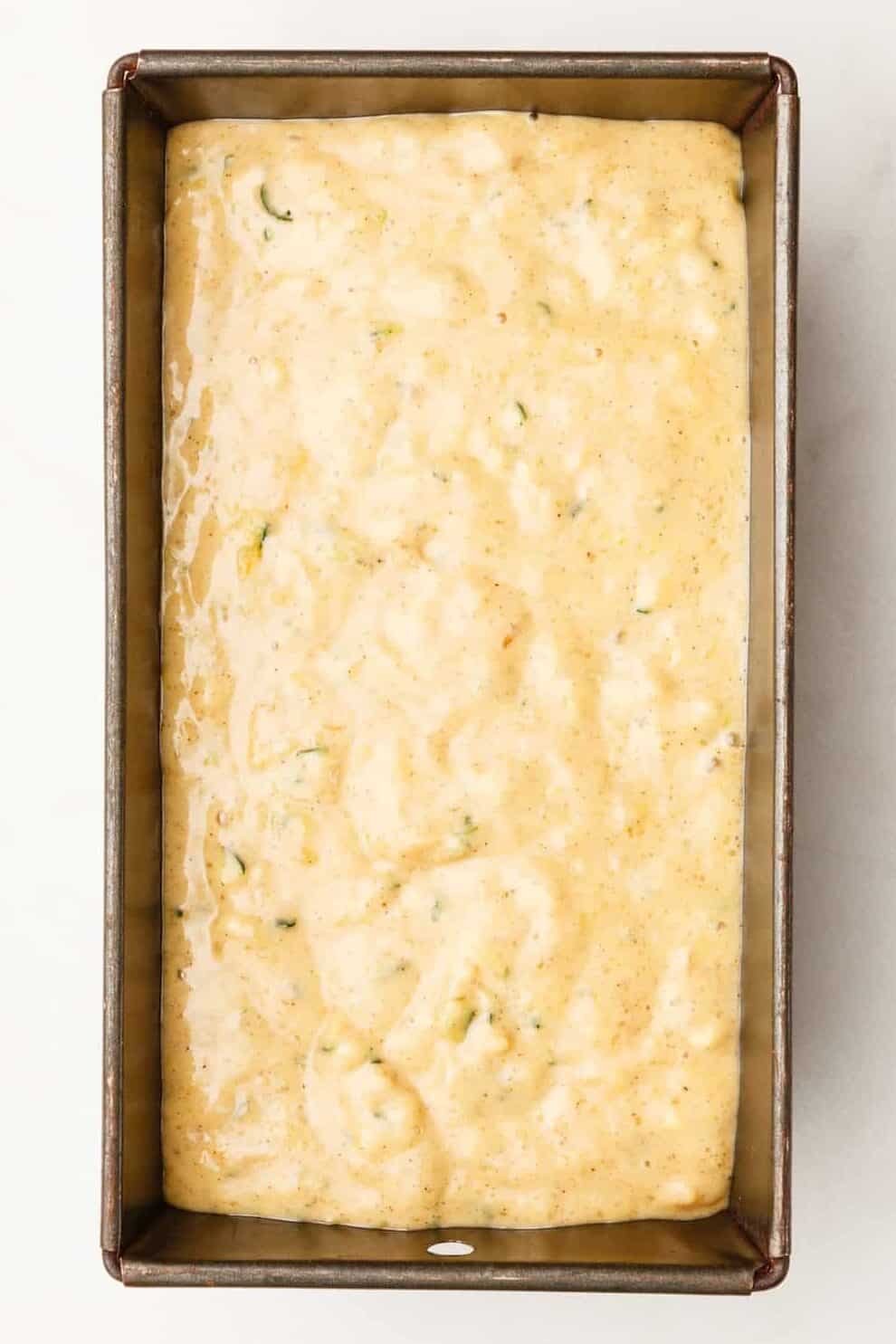 pouring the banana zucchini bread mixture into a loaf pan.