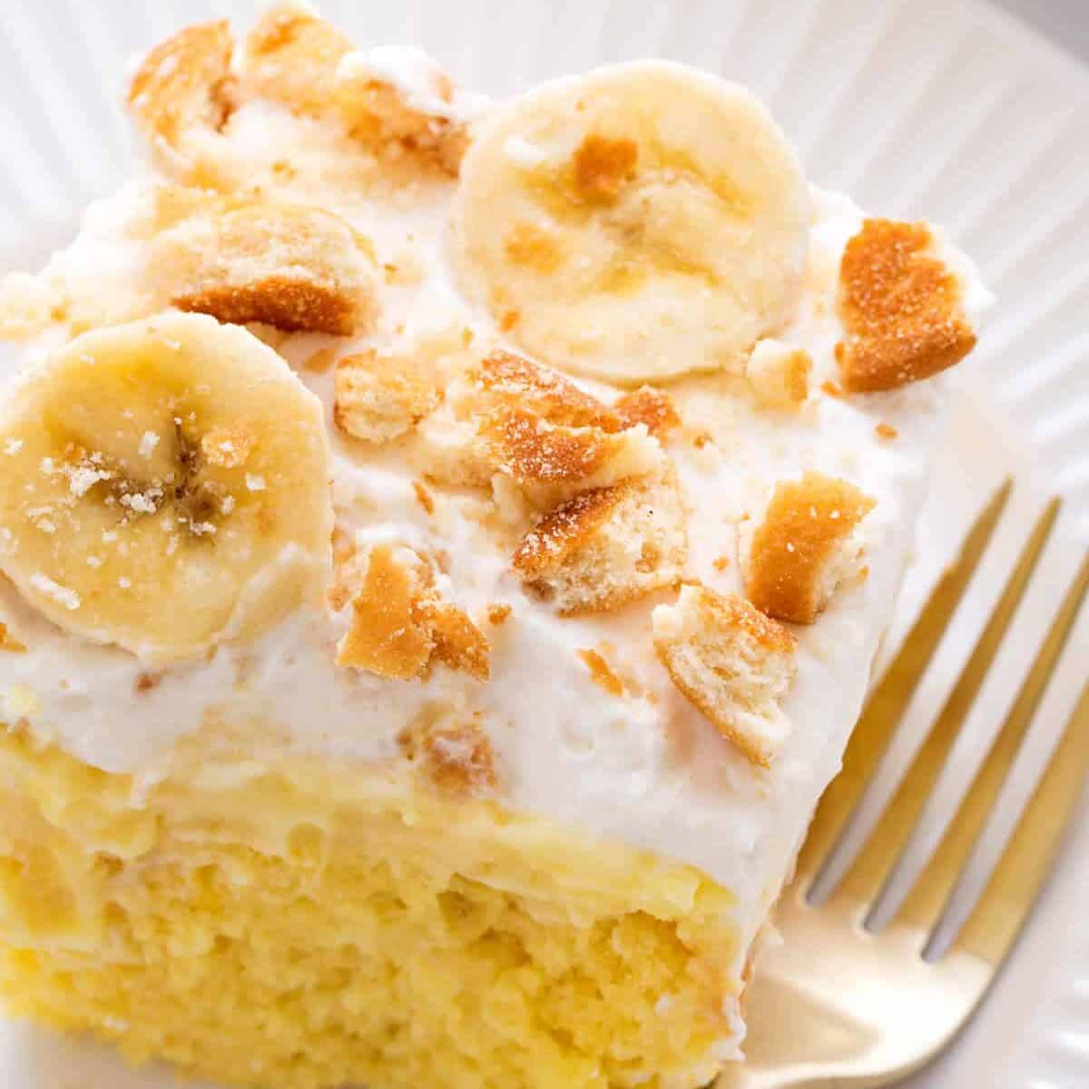 A slice of banana pudding poke cake on a plate with a fork next to it. 