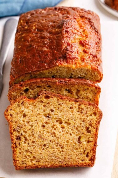 Close up of baked and sliced 4-ingredient banana bread on parchment paper atop a wooden cutting board.