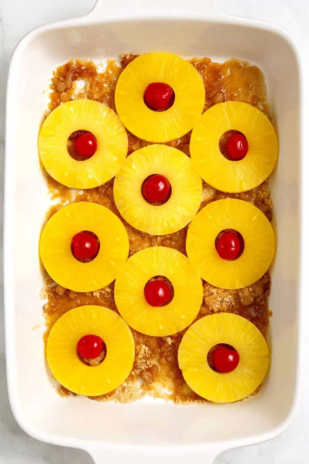pineapple slices with maraschino cherries in baking dish. 