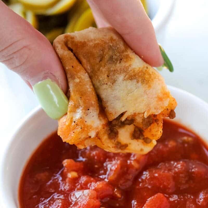 Hand dipping piece of taco stick into marinara sauce held in small white bowl