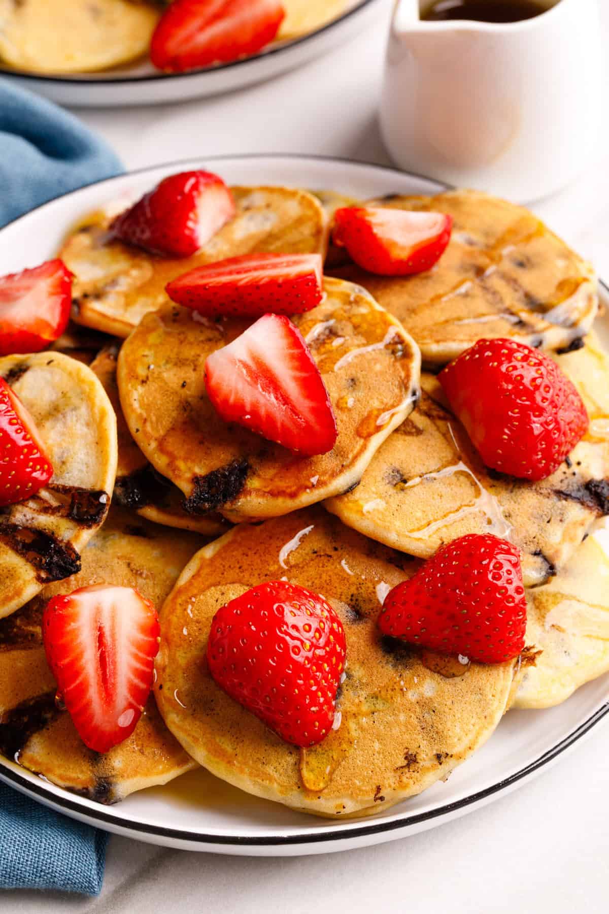 A large plate of mini chocolate chip pancakes, topped with fresh strawberries, and syrup.