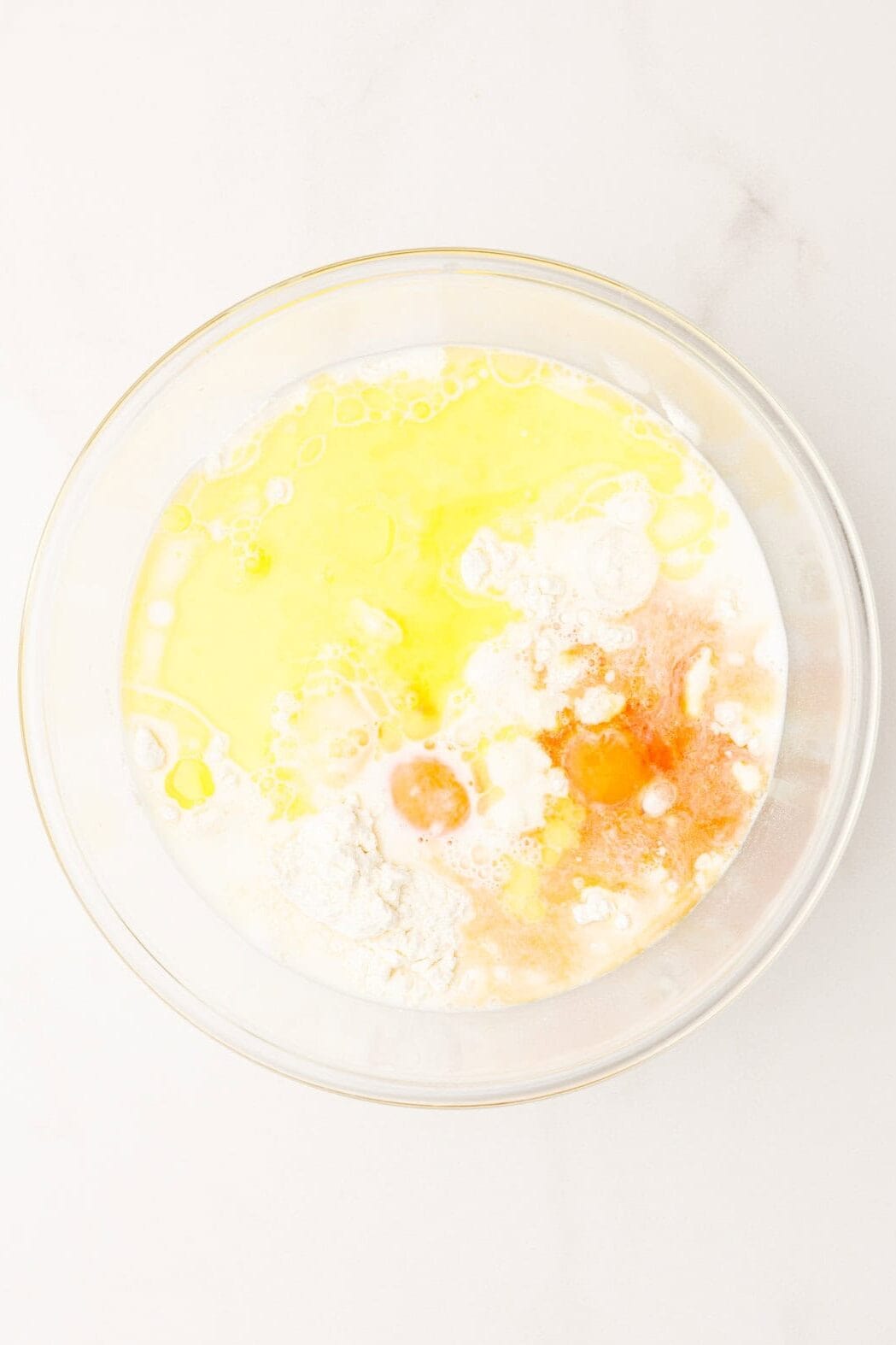 Top image of a large glass bowl with pancake batter ingredients.