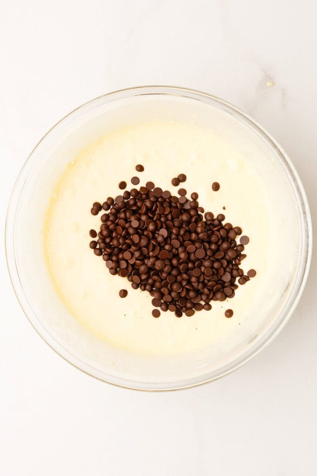 Top down image of a large glass bowl with pancake batter and mini chocolate chips.