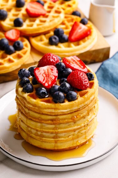 A stack of mini waffles topped with berries and syrup.