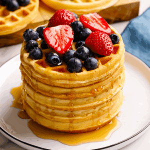 A stack of mini waffles topped with berries and syrup.