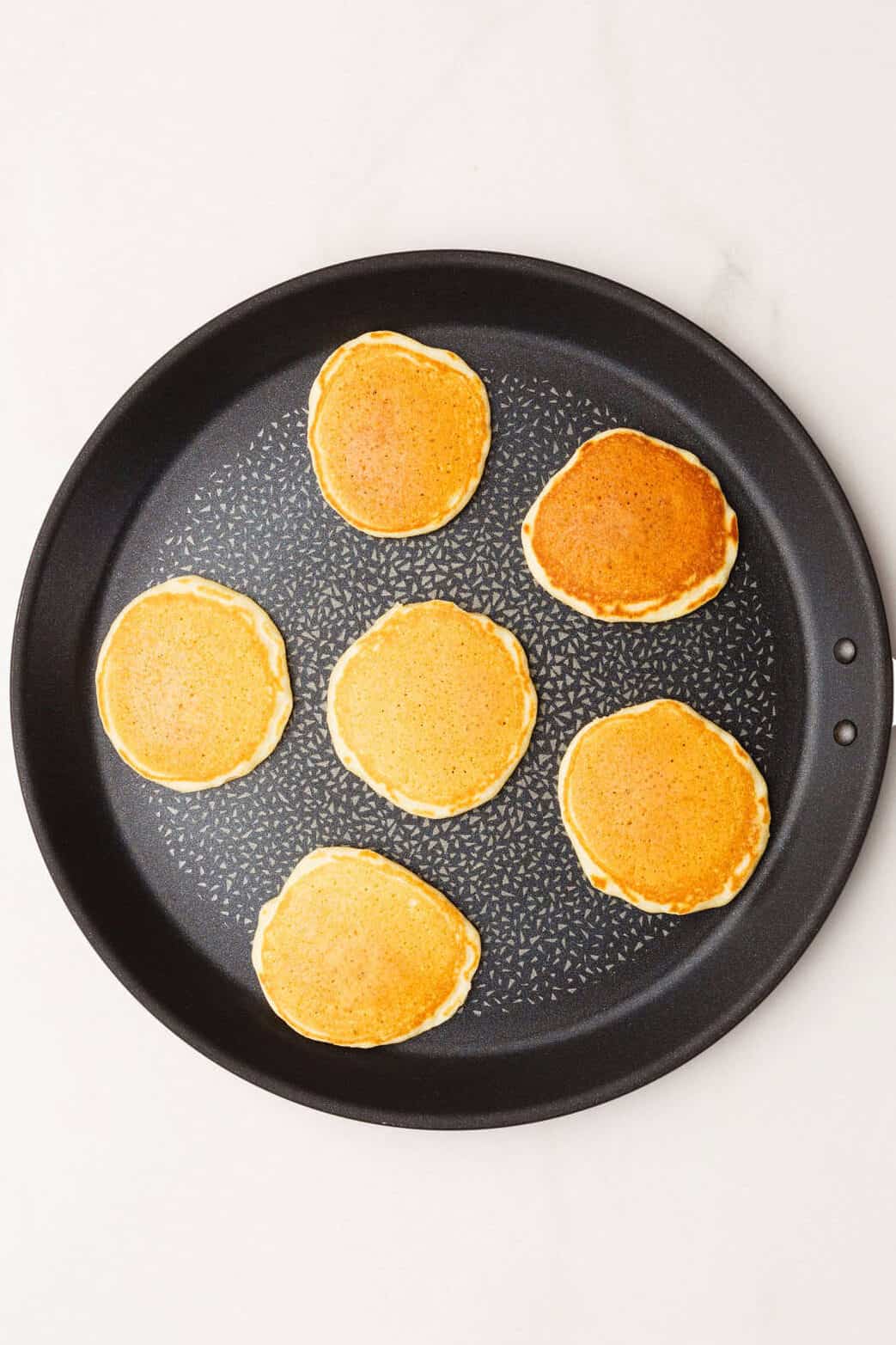 Cooked silver dollar pancakes in a heated skillet with a golden finish. 