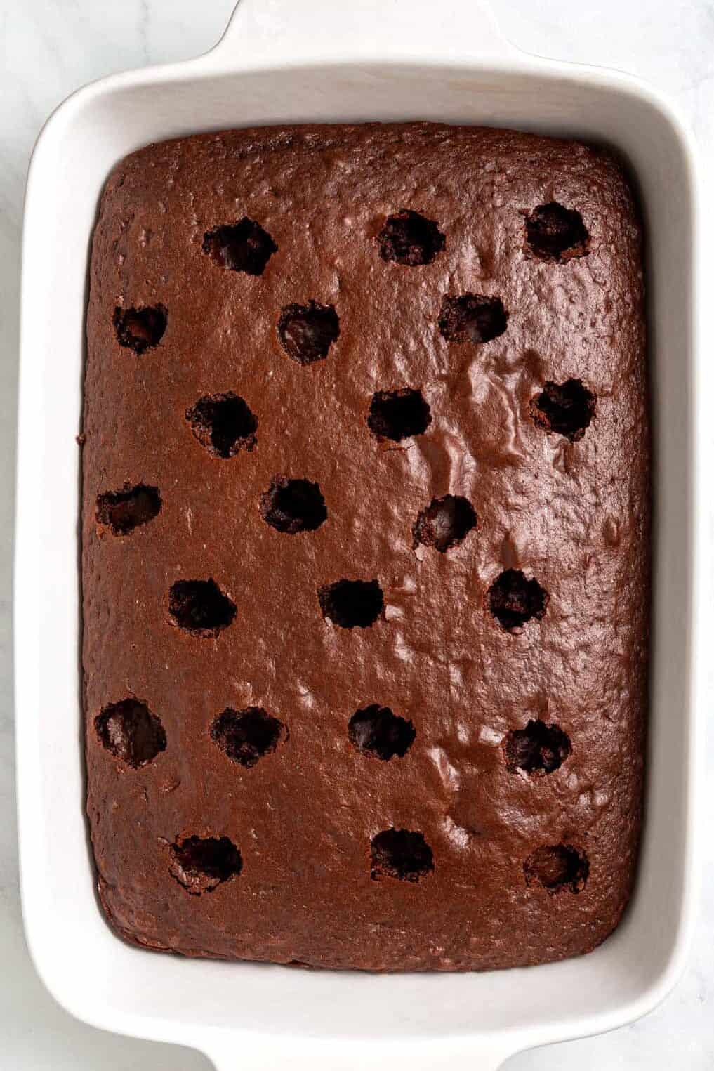 Image of a 9 x 13 casserole baking dish with baked chocolate cake with holes poked in it.