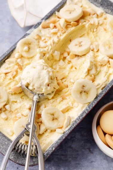 An ice cream scoop holding a scoop of banana pudding ice cream on top of a loaf pan.