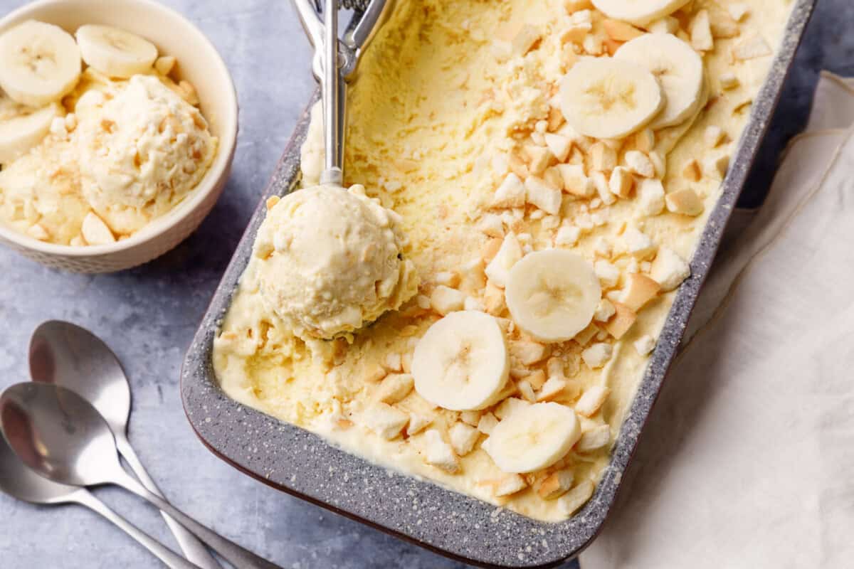 An ice cream scoop lifting a scoop of no churn banana ice cream from a loaf pan.
