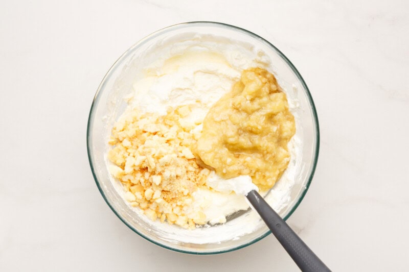Mashed bananas and cookies being stirred into a whipped cream cheese mixture.