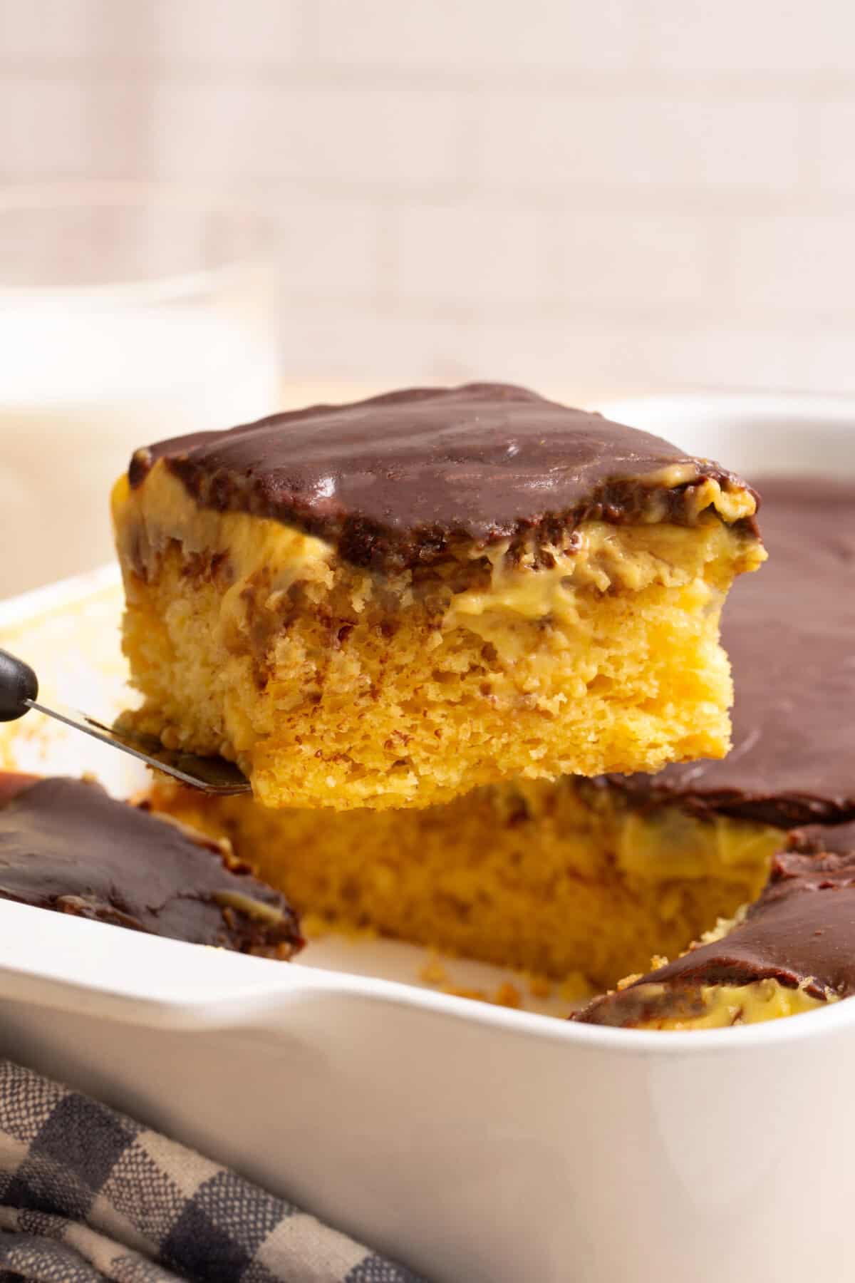 A slice of Boston Cream Poke Cake being lifted from a pan.