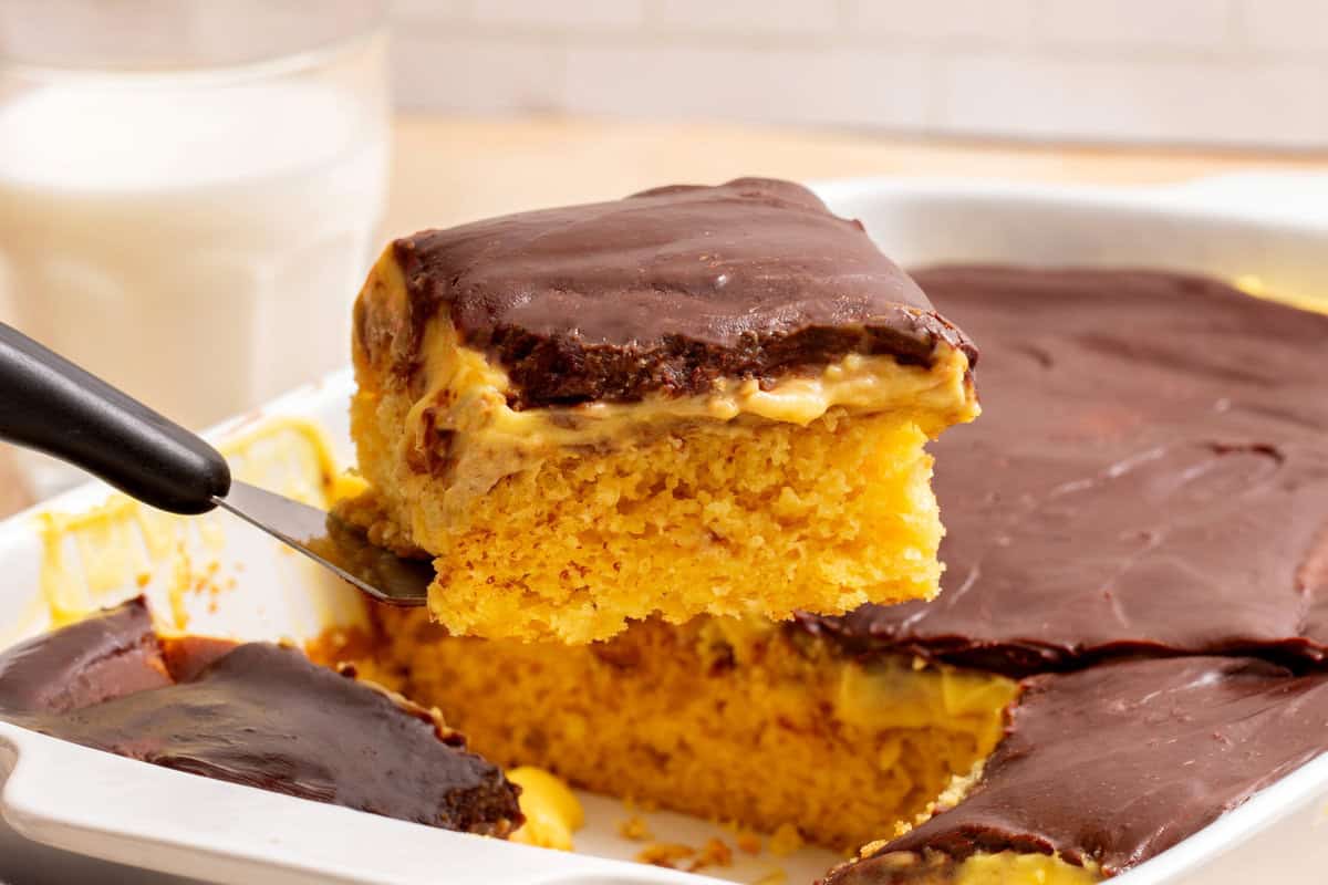 A slice of Boston Cream Poke Cake being lifted from a baking dish.