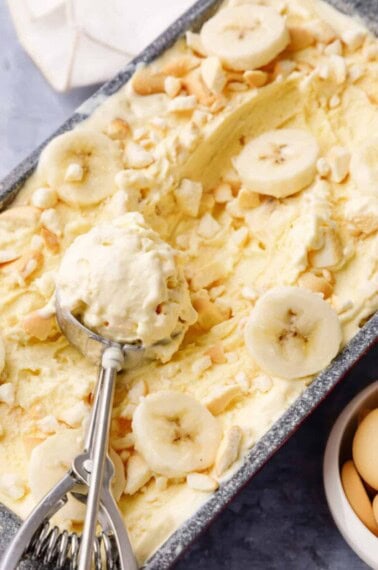 An ice cream scoop holding a scoop of banana pudding ice cream on top of a loaf pan.