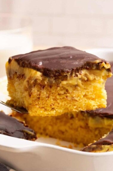 A slice of Boston Cream Poke Cake being lifted from a pan.
