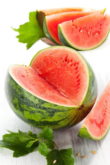 A whole watermelon with a large wedge missing.