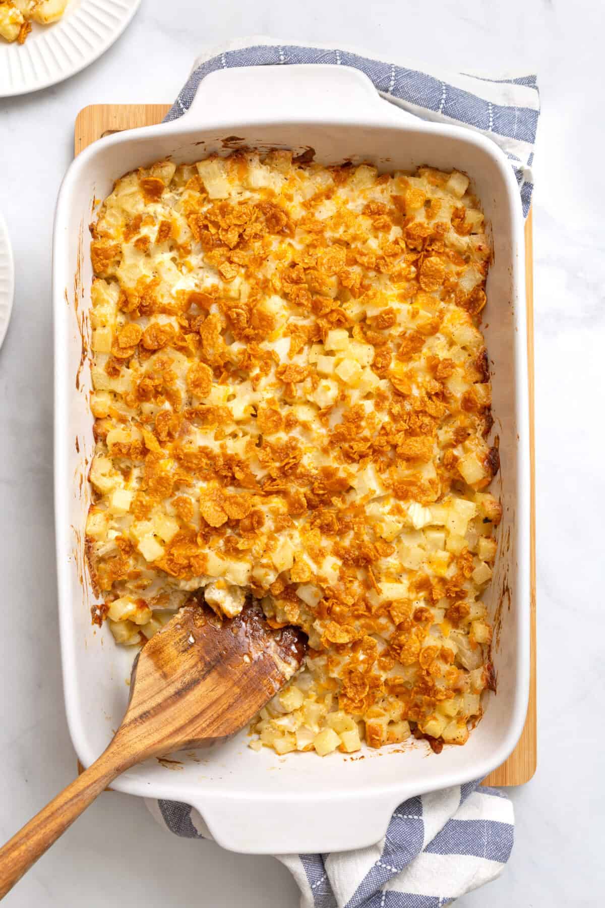 cheesy amish funeral potatoes in a white dish on a wooden cutting board