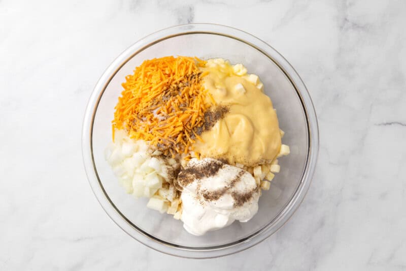 Large glass mixing bowl with thawed hash browns, cream of chicken soup, sour cream, 1/2 cup melted butter, chopped onion, cheddar cheese, salt and pepper.
