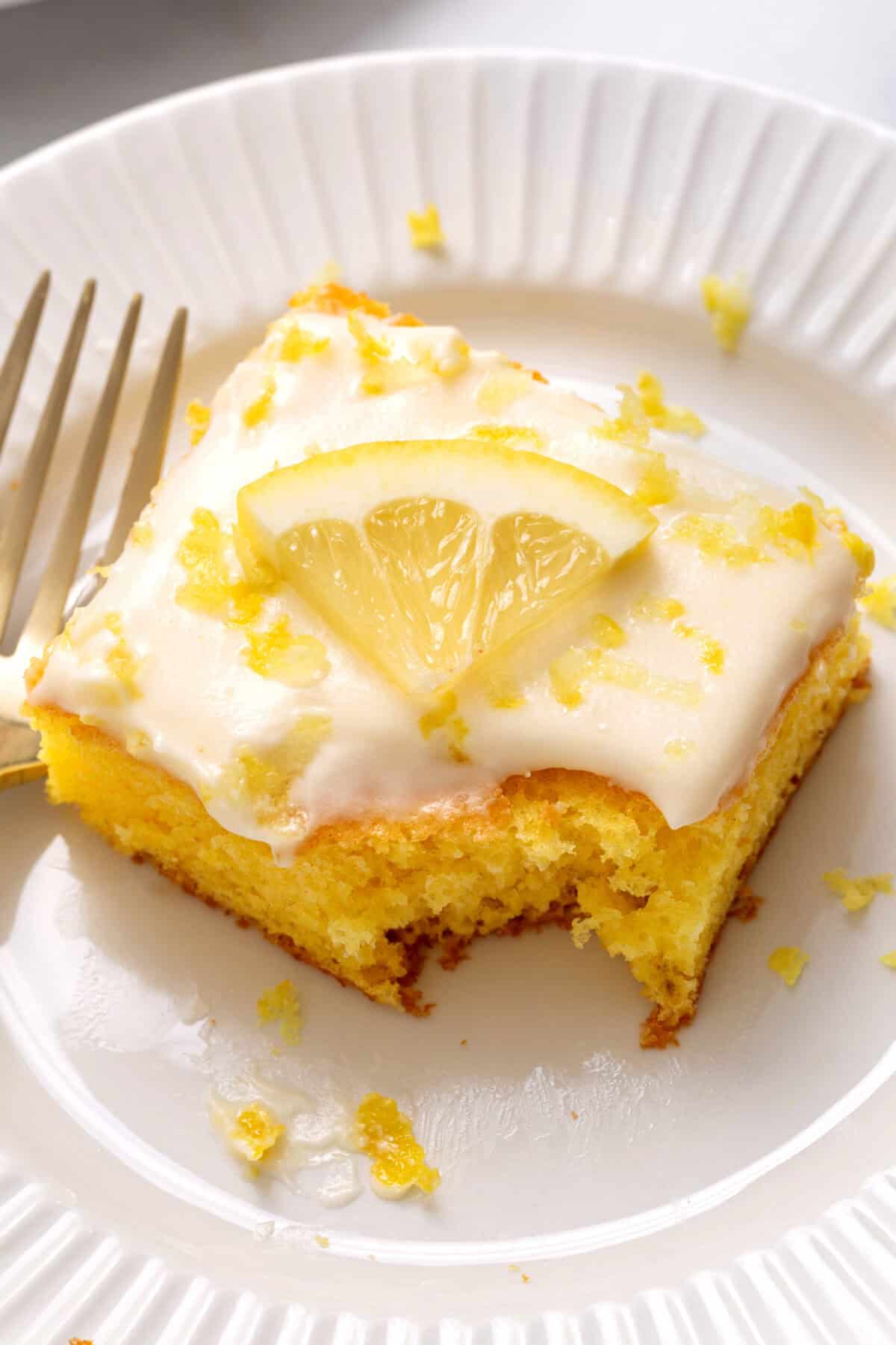 a piece of lemon sheet cake on a white plate with a piece taken out.