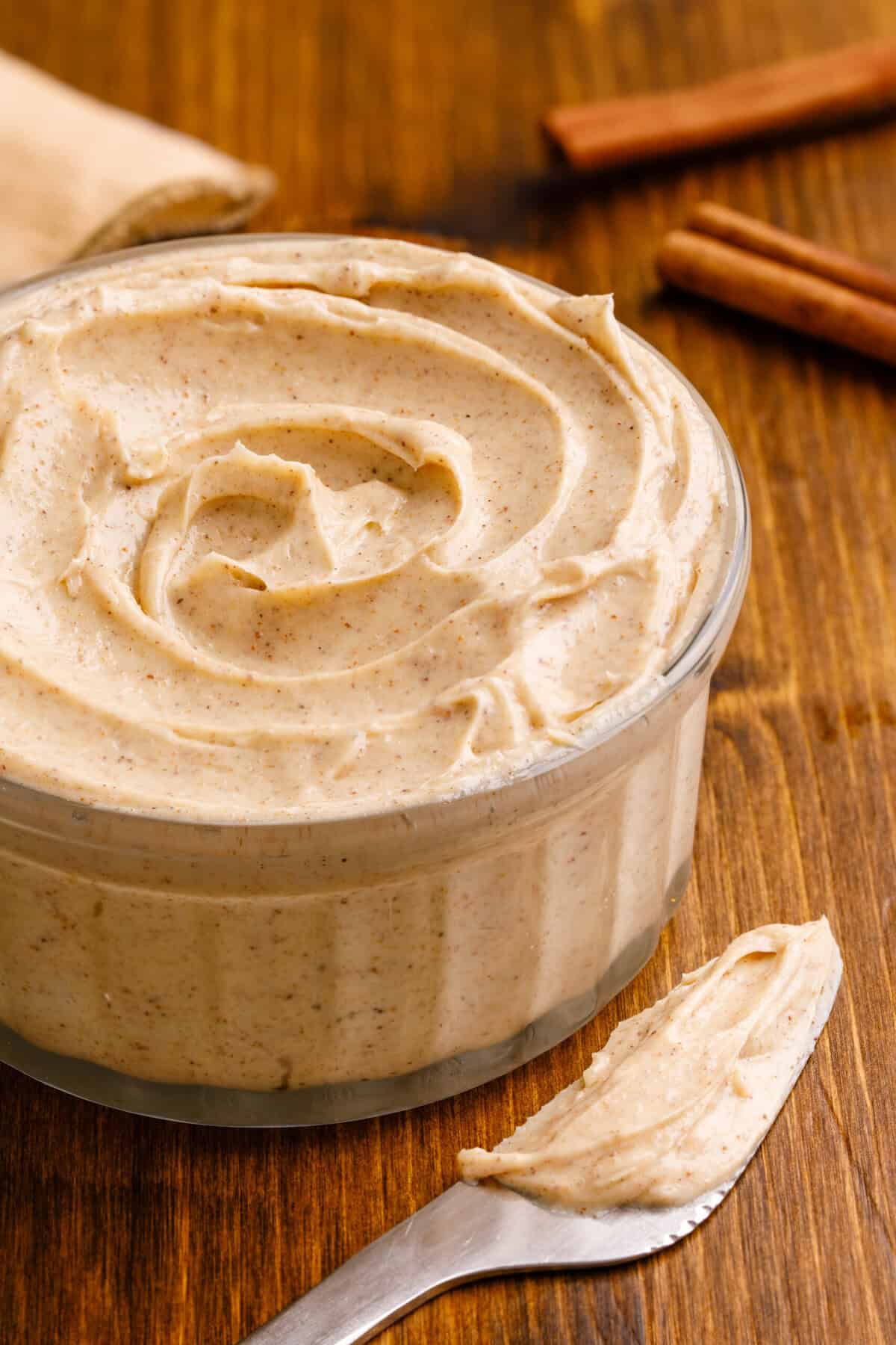 Bowl of freshly whipped cinnamon butter surrounded by cinnamon sticks on a rustic table