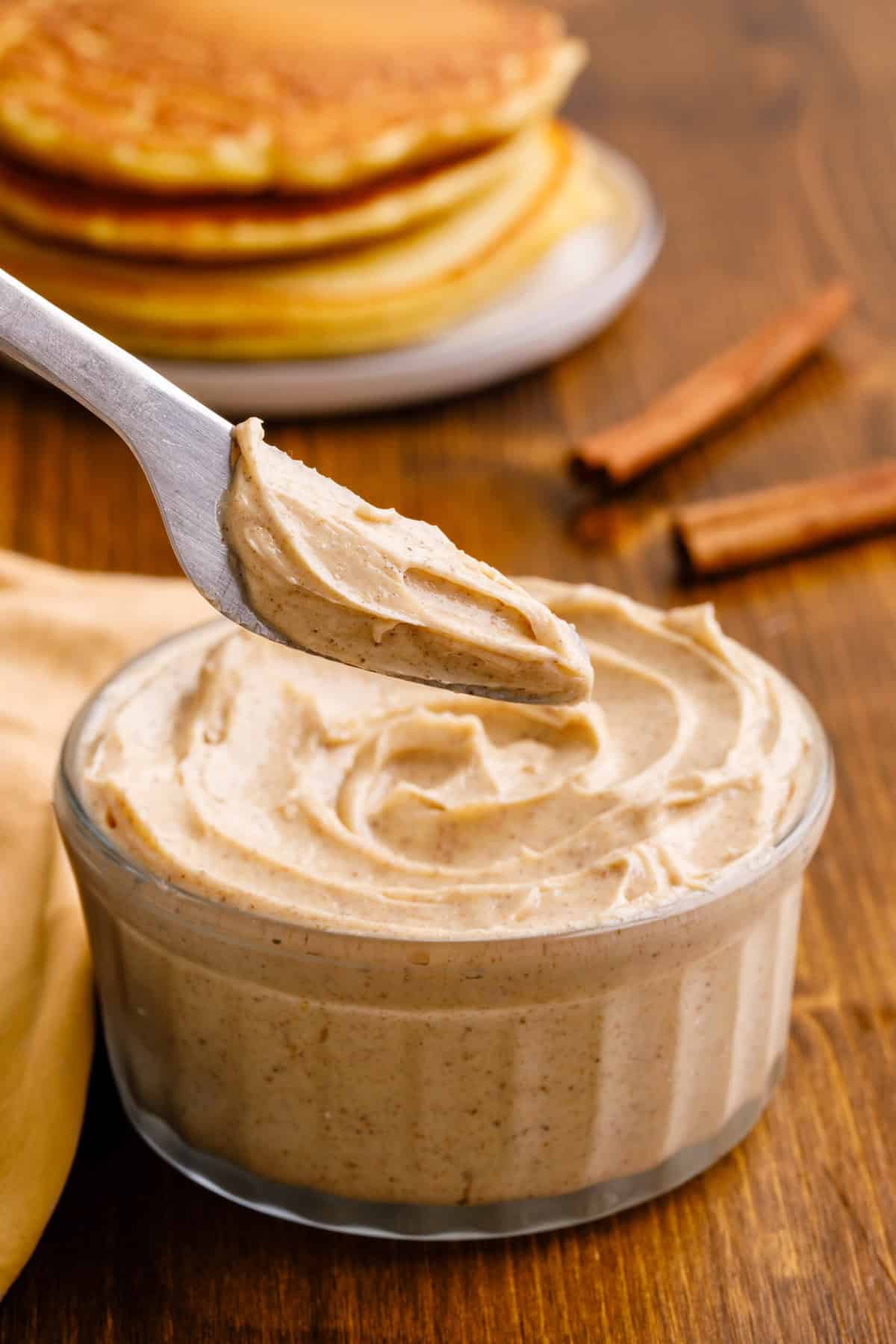 A spreadable knife showing cinnamon butter with a bowl of cinnamon butter with pancakes in the background. 