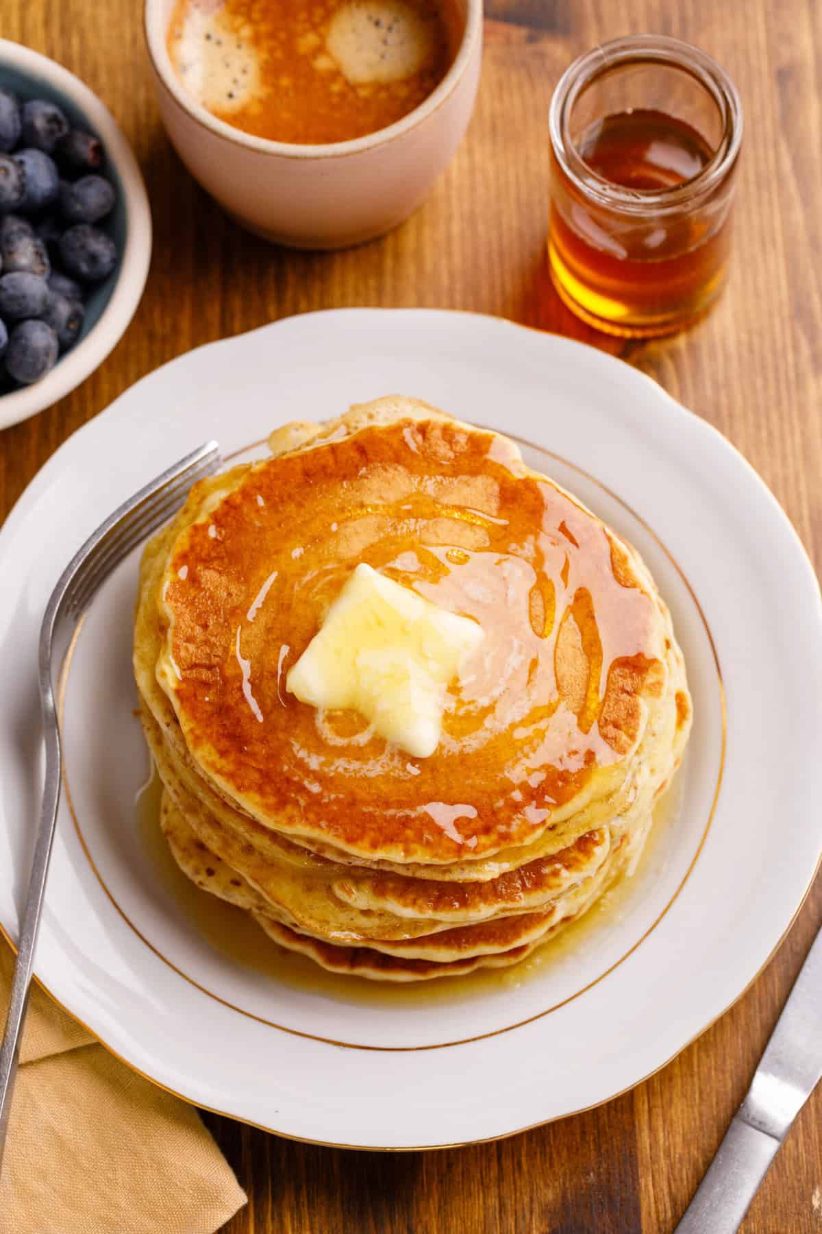 Stack of cracker barrel pancakes  served on a white round plate iwht gold detailing, aerial view.