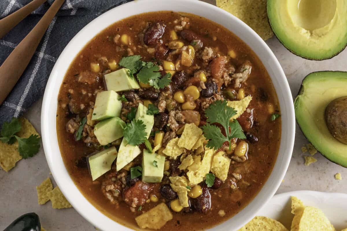 Taco soup made in a slow cooker with avocado and chips.
