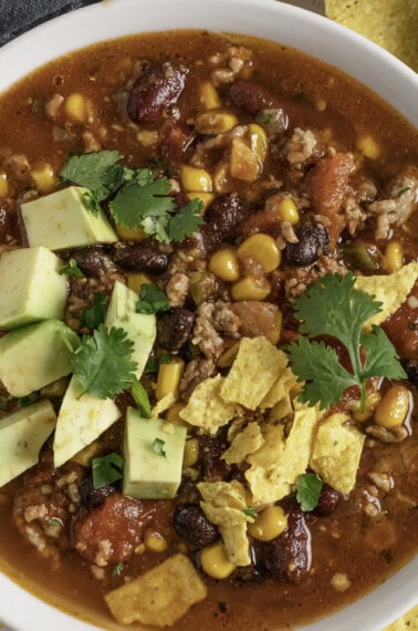 Taco soup made in a slow cooker with avocado and chips.