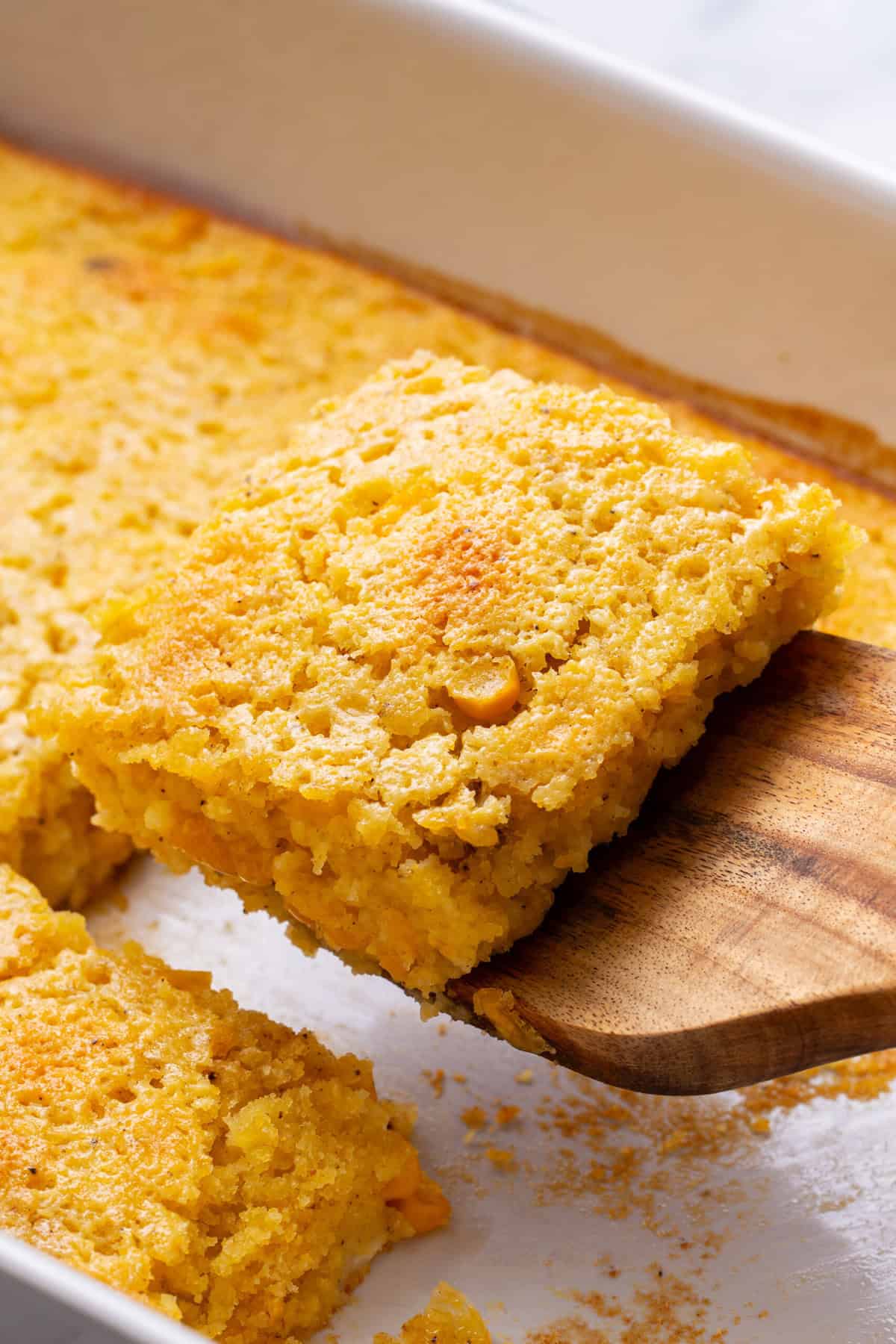 wooden spatula holding a square of corn souffle. 