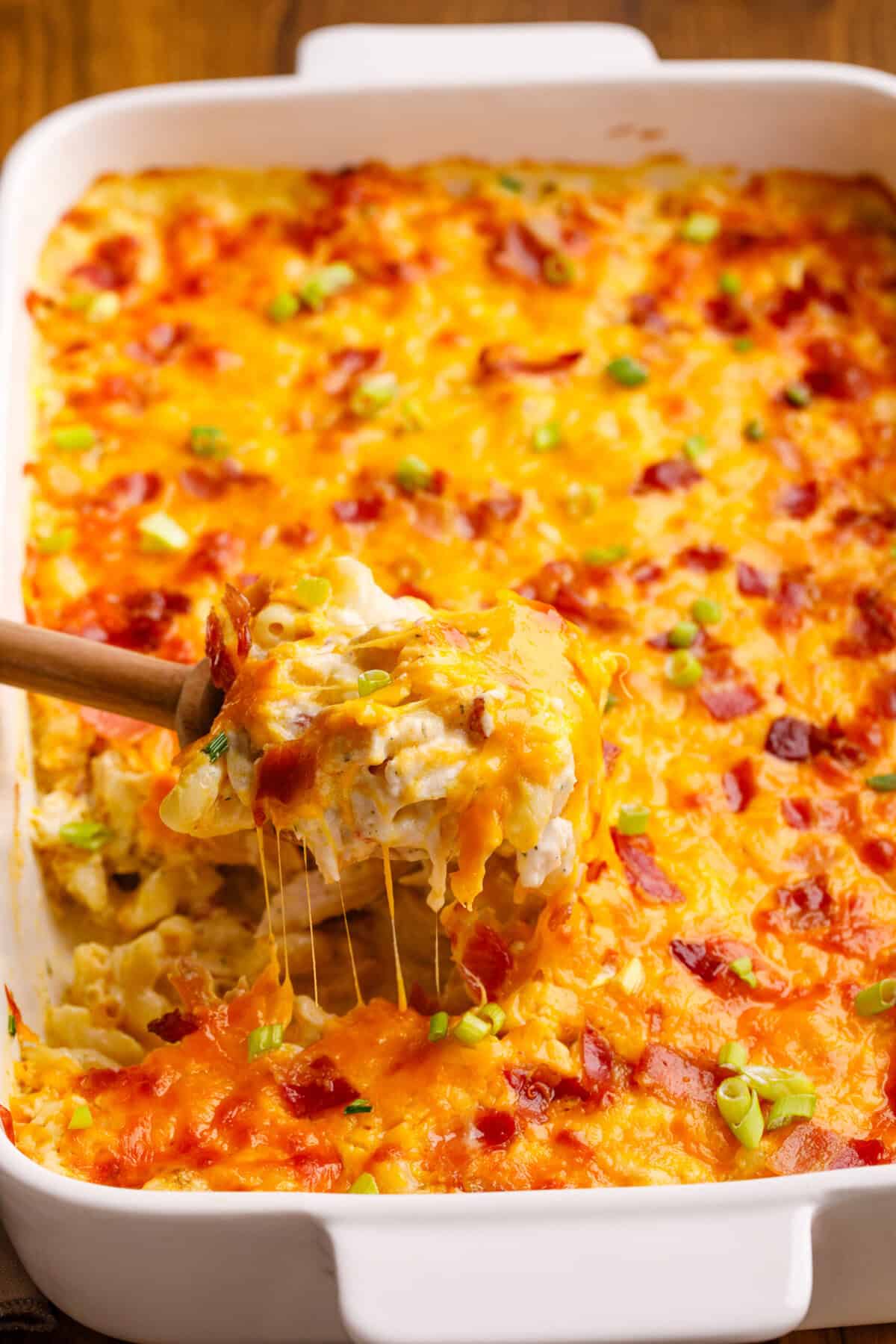 A wooden spoon scooping out a serving of crack chicken casserole. 