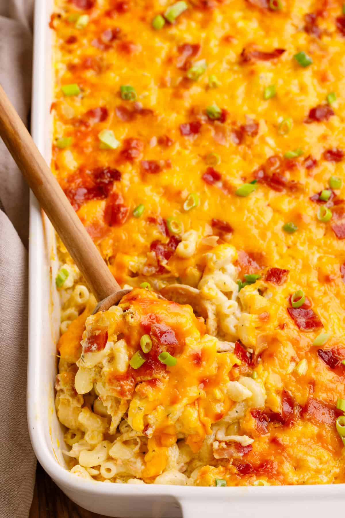 A wooden spoon taken a serving out of crack chicken casserole out of a baking dish. 