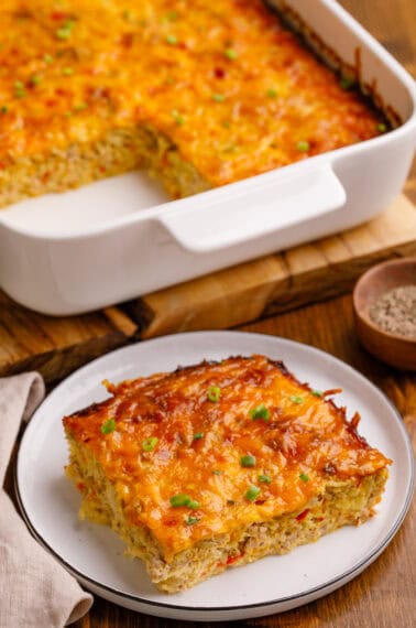 Hashbrown egg casserole on a plate with more in the back in a baking dish.