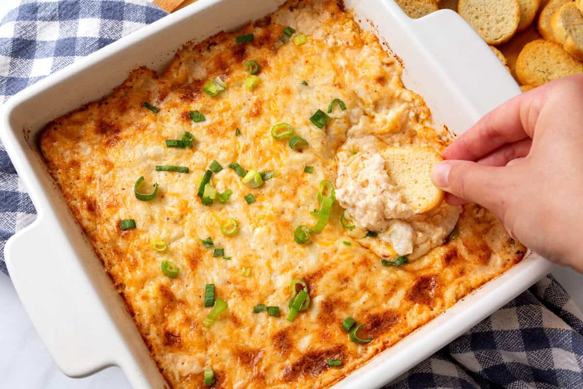 Cracker dipping in freshly baked hot crab dip. 