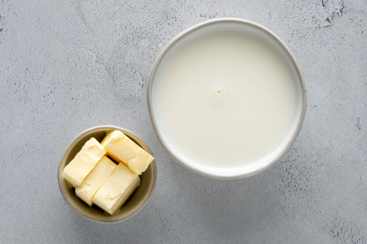 Milk and butter in bowls on a stone surface.