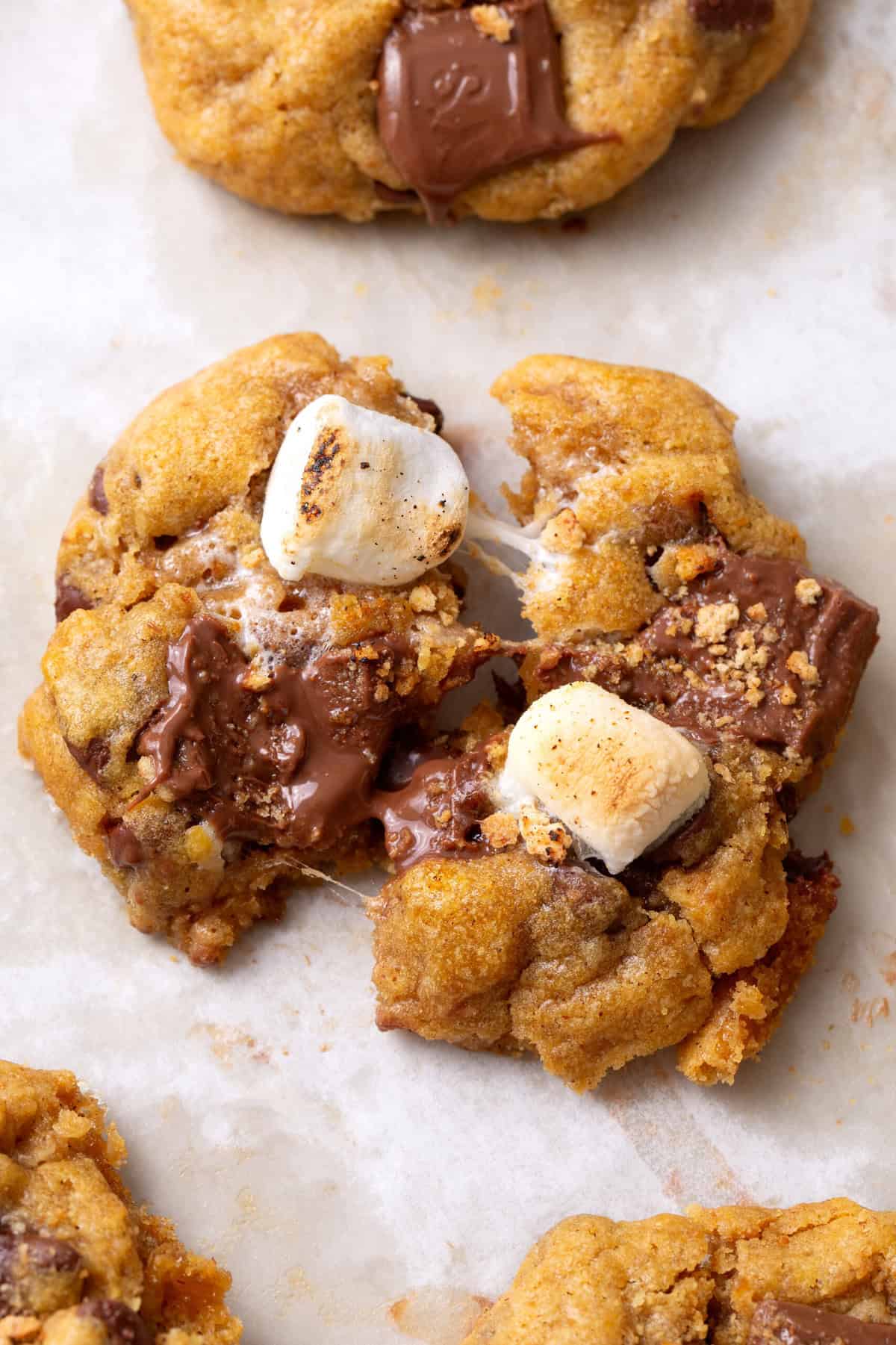 pumpkin smores cookie Close-up of a Pumpkin S'mores Cookie broken in half, showing a gooey marshmallow and chocolate-filled center with graham cracker crumbs