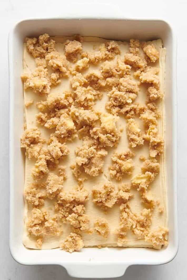 cinnamon crumble on top of crescent roll dough and cheesecake filling in a 9x13 casserole dish