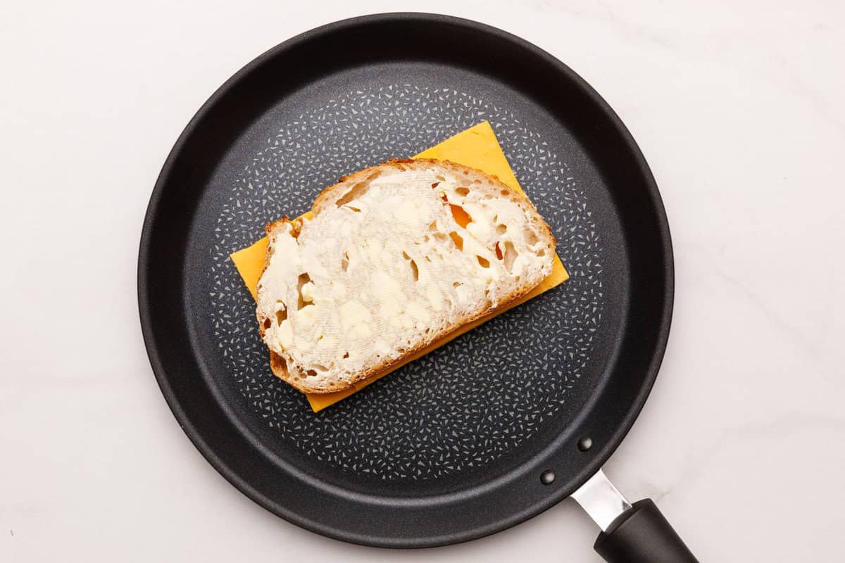 A piece of bread on top of cheese for a Grilled Cheese Sandwich. 